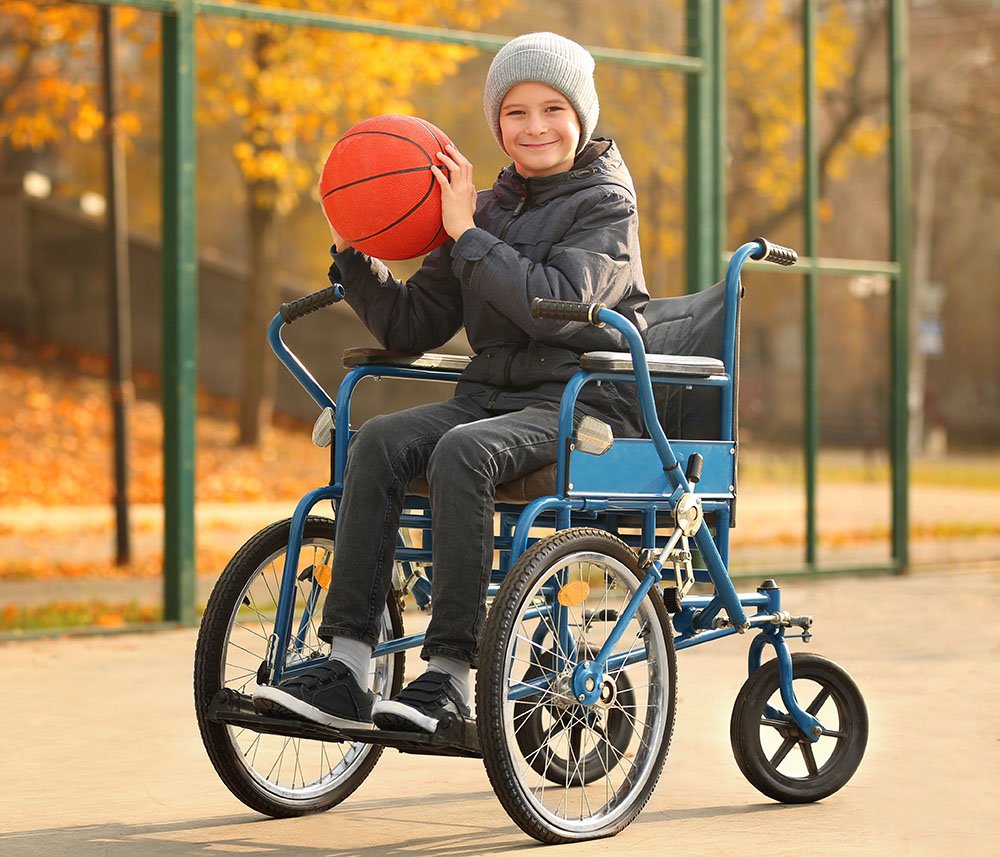 Little boy in wheelchair with ball on playground