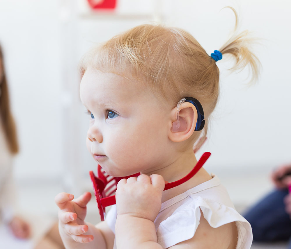 Hearing aid in baby girl's ear. Toddler child wearing a hearing aid at home. Disabled child, disability and deafness concept.